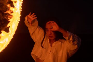 a woman in white long sleeves and skirt dancing near the fire