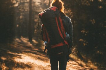 unrecognizable woman with backpack walking in forest