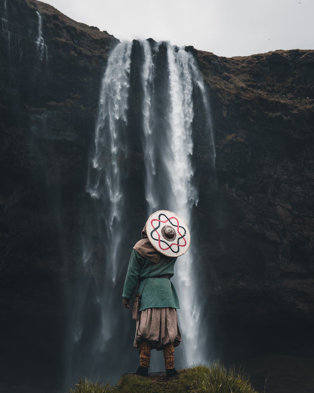 person in warrior clothes standing and looking at waterfall
