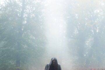 person wearing a black hooded cape standing on a field