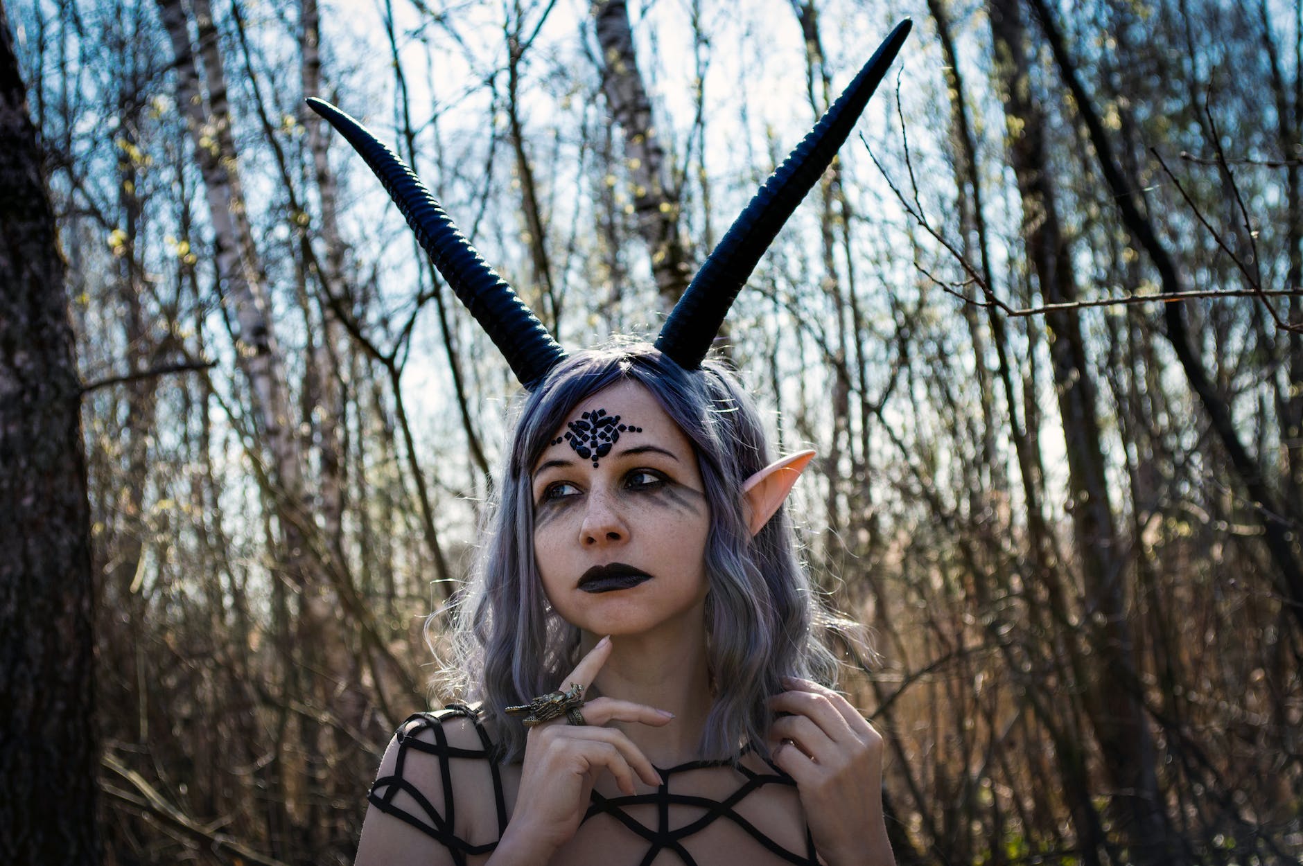 young female in dark costume with horns in woods